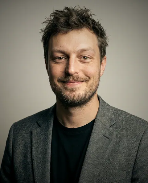Retrato de Tomek Kubiak, Engenheiro front-end do Pollyfriends, sorrindo em fundo cinza claro